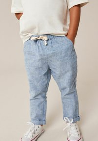 Lysblå bukser i en linned og bomuldsblanding med elastisk talje og beige snor, med opsmøgte bukseben og sidelommer, parret med hvide sneakers.