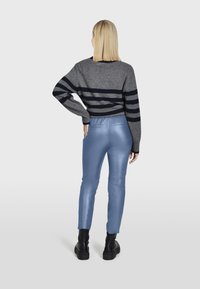 Grijze en marineblauwe gestreepte trui gecombineerd met blauwe glanzende faux leren broek en zwarte chunky boots. De trui heeft een relaxte pasvorm en geribde manchetten.