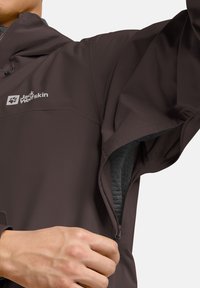 Brązowa wodoodporna kurtka z zamykanym na zamek kieszonką, lekkim materiałem, regulowanym kapturem oraz logo na klatce piersiowej. Płaskie szwy i gładka tekstura.