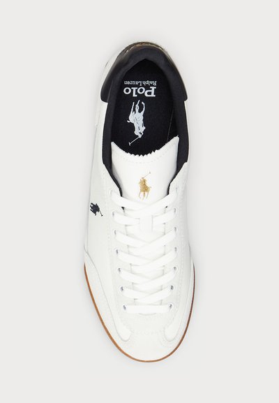 Vit sneaker med överdel i canvas, svart foder och guldlogotyp. Har en gummisula och flera snören för en säker passform.