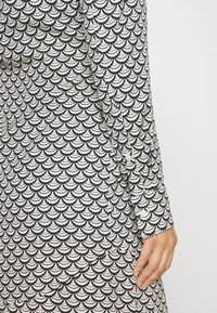 Long-sleeved dress featuring a black and white scallop pattern, made from lightweight fabric with a smooth texture and buttoned cuff detail.