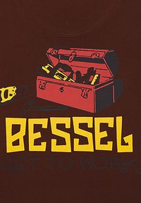 Camiseta marrón de manga corta con un gráfico de una caja de herramientas abierta con varias herramientas, encima de un texto en negrita amarillo que dice "BESSEL PÓNTE A TRABAJAR."