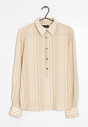 Chemise beige à manches longues avec boutons, rayures verticales, col pointu et poignets, suspendue à un cintre noir sur un fond blanc.