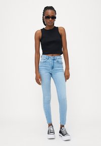 Črn skrajšan top brez rokavov, svetlo modri zgoraj podloženi skinny jeans in črne platforme z belimi podplati. Eleganten dizajn z minimalnim okrasjem.
