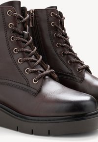 Barna bőr bokacsizma kerek orral, fényes fém fűzőlyukakkal, fűzős elülső résszel és oldalsó cipzárral; texturált felület és vaskos fekete talp.
