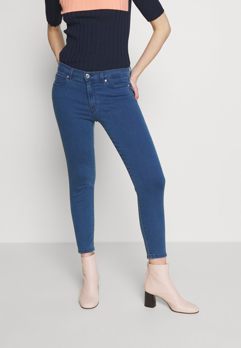 Jeans ajustados de mezclilla azul con una textura suave y diseño de cinco bolsillos, combinados con botines rosa claro con tacón bloque.
