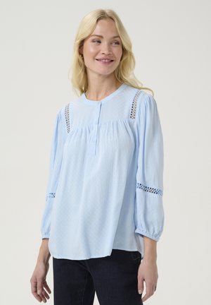 Blusa azzurro chiaro con scollatura rotonda, patta di bottoni, tessuto testurizzato e dettagli in pizzo su spalle e maniche. Vestibilità comoda.