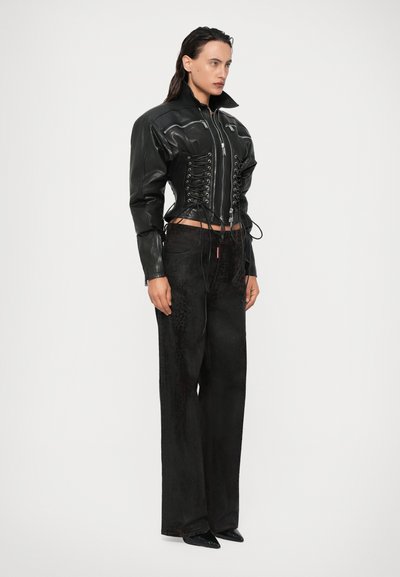 Sort læderjakke med korsettelignende snøring i taljen, parret med løstsiddende sorte jeans med en subtil tekstur og mønster.
