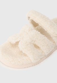 Crèmerfarbenes, flauschiges Sandalenpaar mit zwei breiten Riemen und einem unterstützenden Fersenriemen auf einer flachen Sohle.