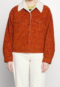 Hnědočervená kordurová bunda s bílým umělým šerlingovým límcem, knoflíkovým zapínáním a dvěma náprsními kapsami. Uvolněný střih a texturovaná látka.