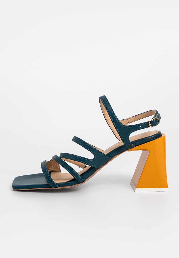 Sandale en cuir teal avec un bout carré et trois larges brides. Elle présente un talon bloc avec un design géométrique aux accents orange et blanc.