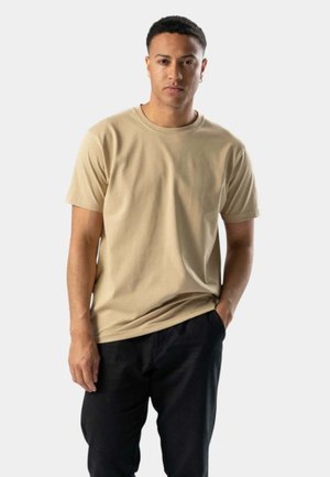 Beige bomulds T-shirt med rund hals og kort ærmer, parret med sorte bukser. Simpelt design med en afslappet pasform og glat tekstur.