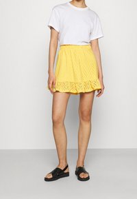 Geel geborduurde rok met een golvende zoom, voorzien van een textuurdesign, gecombineerd met een witte t-shirt en zwarte sandalen.
