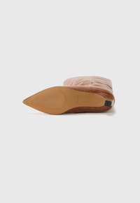 Chaussure plate à bout pointu en cuir texturé marron. Présente un dessus lisse avec de légères lignes verticales et une semelle en caoutchouc beige.