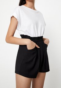 T-shirt blanc à manches courtes associé à un short noir taille haute avec une ceinture élastique et des poches latérales, texture de tissu lisse.