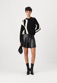 Black and cream striped sweater with long sleeves, paired with a black pleated leather skirt. Model holds a small black handbag. Black ankle boots.