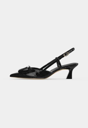 Chaussure slingback à talon kitten en cuir verni noir avec bout pointu et boucle décorative à l'avant sur fond blanc.