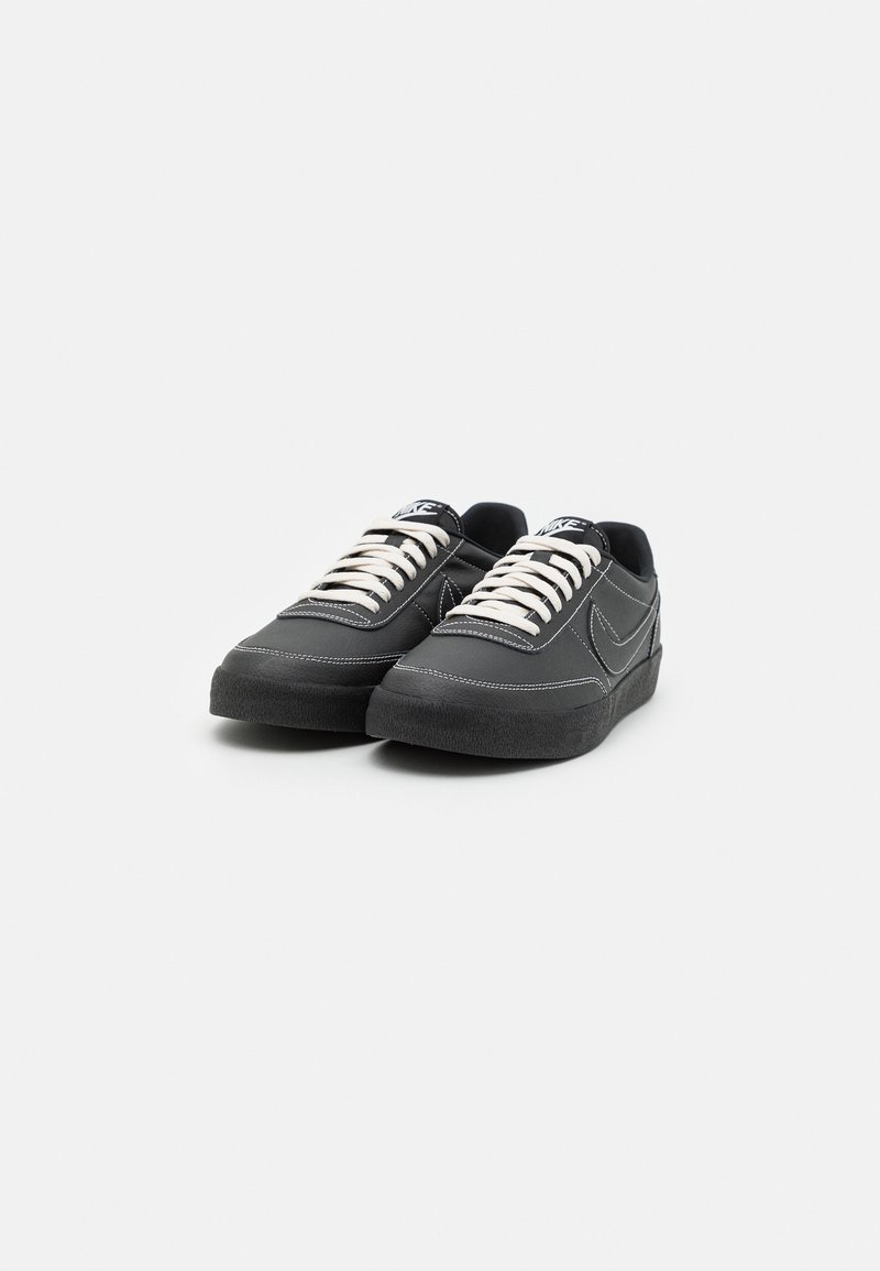 Zapatillas negras con cordones blancos, upper de cuero suave, puntera redondeada y suela de goma negra texturizada. Acentos de costura blanca en todo.