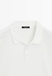 Bílá polo košile vyrobená z hladké bavlny s klasickým límcem, tříknoflíkovou légou a štítkem označeným "Massimo Dutti" na výstřihu.
