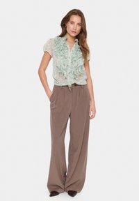 Ljusgrön volangblus med korta ärmar, knappslå och blommönster. Bruna vida byxor med plisserad framsida och midja.
