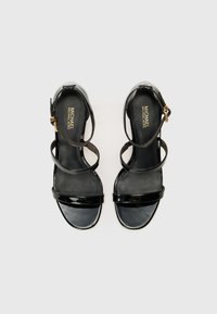 Sandales à talons hauts en cuir verni noir, dotées de deux fines brides de cheville, d'une large bride à l'avant et d'une finition lisse et brillante. Accent en métal doré.
