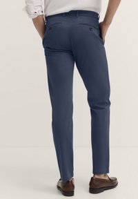 Marineblaue Slim-Fit-Hosen mit einem glatten Gewebe, ausgestattet mit zwei Gesäßtaschen mit Knopfverschluss und einem leicht taillierten Beinverlauf.