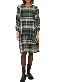 Langärmliges kariertes Kleid in Grün, Schwarz und Creme; verfügt über einen runden Ausschnitt, einen gerafften Saum und eine lockere Passform. Kombiniert mit schwarzen Knöchelstiefeln.
