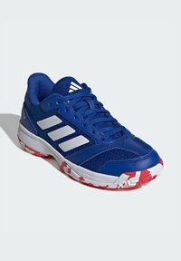 Chaussure de sport bleue avec tige en maille et en cuir synthétique, design à trois rayures blanches, semelle intermédiaire texturée et semelle extérieure avec motif camouflage rouge.