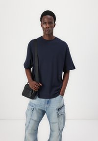Tricou bleu marin cu mânecă scurtă, cu o croială lejeră, asortat cu blugi cargo de culoare albastru deschis, dotati cu buzunare și fermoare. O mică geantă crossbody neagră completează ținuta.
