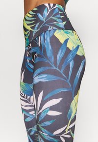 Blommönstrade leggings i mörkgrått med gröna och blå bladmönster. Slät tyg med hög midja och åtsittande design.