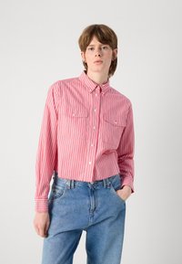Randig skjorta i röd och vit med två bröstfickor, långa ärmar och krage, i kombination med blåjeans.