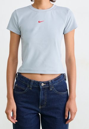 Femme portant un t-shirt Nike court bleu clair et un jean bleu foncé sur fond blanc uni.
