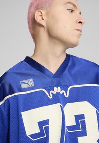 Jersey de malla azul con acentos blancos, con un diseño de cuello en V, gran número 72 y un pequeño logo de Puma en el hombro.