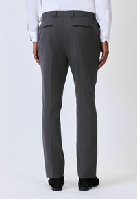 Pantaloni gri personalizați, dintr-un material texturat, cu buzunare pe spate cu accente negre și croială dreaptă. Purtați cu pantofi negri.
