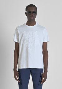 Witte katoenen t-shirt met een getextureerde tijgerafbeelding gedrukt op de voorkant, ronde hals en korte mouwen. Gecombineerd met donkere cargobroeken.