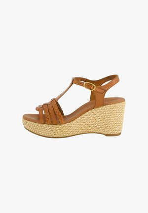 Sandal de cuña de cuero marrón con correas trenzadas y una plataforma de fibra natural texturizada. Presenta una correa de tobillo ajustable con un hebilla dorada.