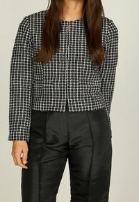 Svart och vit rutmönstrad kort jacka med långa ärmar, rund halsringning och krokstängning. Tillsammans med eleganta svarta höga byxor.