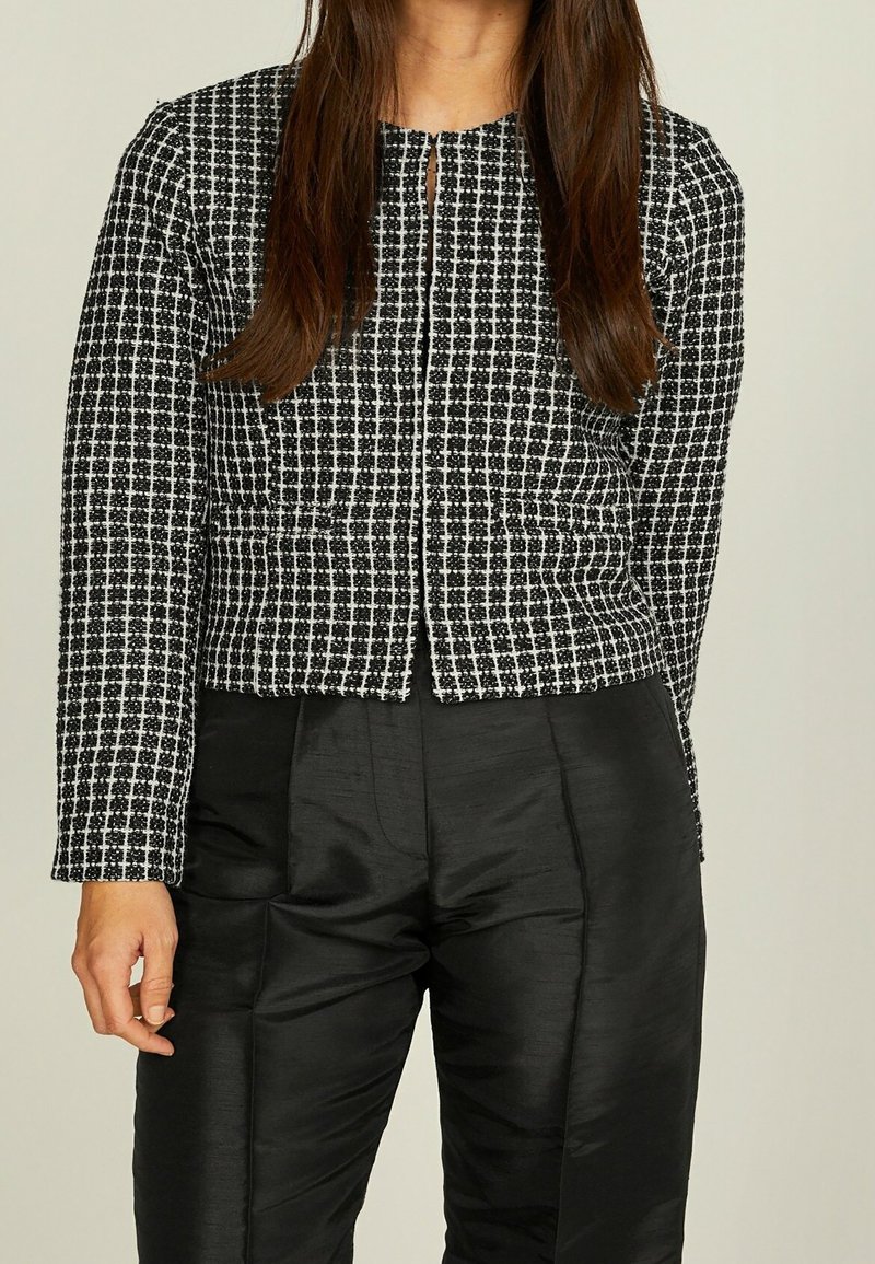 Svart och vit rutmönstrad kort jacka med långa ärmar, rund halsringning och krokstängning. Tillsammans med eleganta svarta höga byxor.