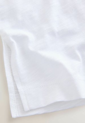 Tissu en coton blanc avec une texture lisse, présentant un ourlet propre et des variations subtiles dans le tissage. Drapeau doux, principalement centré sur le bord.