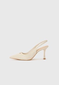 Scarpe con tacco alto beige a scomparsa, con punta affusolata e dettagli ritagliati sottili. Materiale sintetico liscio con tacco snello e suola marrone chiaro.