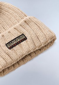 Gorro de punto beige con hilo grueso, que presenta un dobladillo y una etiqueta de logo rectangular en negro y naranja cosida.