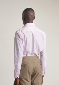 Camisa de rayas rosa claro con cuello clásico, mangas largas y puños abotonados, combinada con pantalones beige de textura suave.