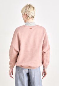 Felpa rosa con una vestibilità rilassata e un aspetto testurizzato, con un piccolo etichetta sul retro, abbinata a pantaloni a righe.