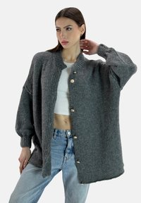 Cardigan grigio lavorato a maglia con una texture a coste, colletto rotondo e bottoni dorati, presenta spalle cadute e una vestibilità oversize.
