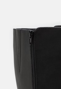 Czarna skórzana torba o fakturowanej powierzchni, wyposażona w zamknięcie na zamek błyskawiczny i gładkie akcenty, prezentująca prosty, uporządkowany design.