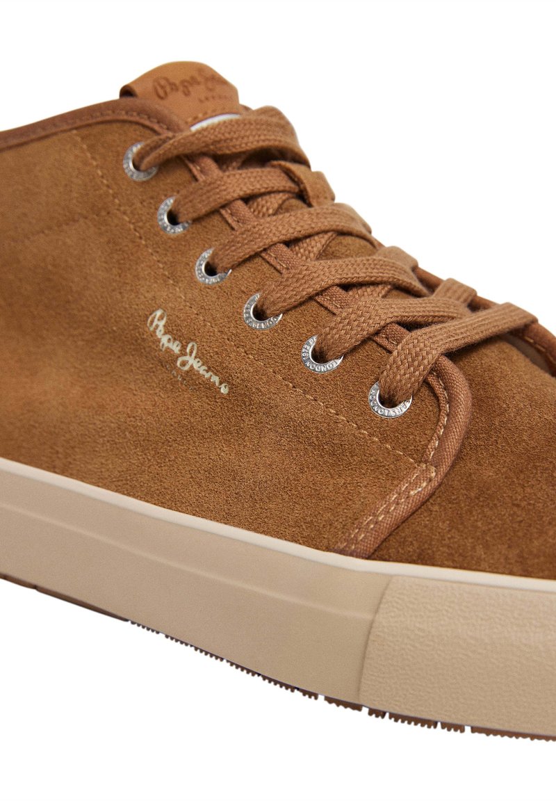 Zapatillas de ante marrón con cordones tono sobre tono, ojales plateados y una suela de goma texturizada beige. Logo "Pepe Jeans" en blanco en el lateral.