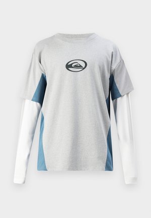 Chemise grise à manches courtes avec de longues manches blanches, présentant des panneaux latéraux bleus et un logo noir sur la poitrine. Matière en coton.