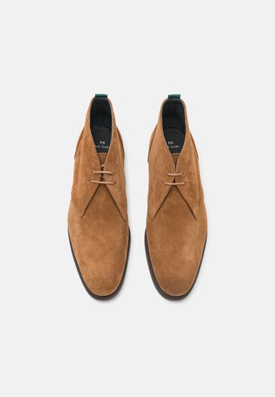 Bruine suède desert boots met een strak ontwerp, met een ronde neus, twee veterogen en een groene hielkap voor accent.