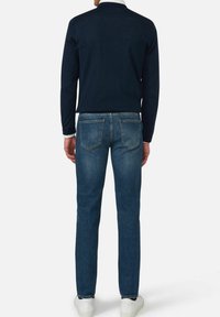 Granatowa koszula z długim rękawem w połączeniu z niebieskimi dżinsami, o klasycznym kroju, z dwiema tylnymi kieszeniami i białymi trampkami. Gładka tekstura materiału.