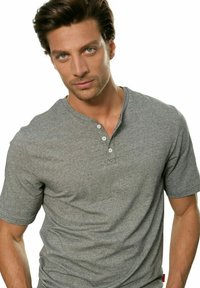 Graues kurzärmeliges Henley-Shirt aus weichem Stoff, mit einer geknöpften Knopfleiste und subtilen Nähdetails, sowie einem Markenetikett am Saum.